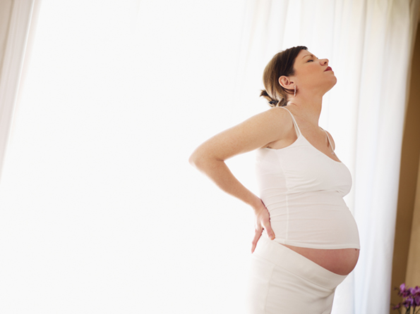 italian 7 months pregnant woman massaging her back. Horizontal shape, side view, copy space